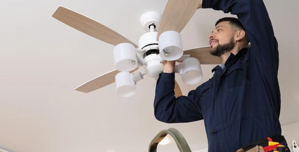 Technician installing a ceiling fan in a home in Deerfield Beach, FL, demonstrating expertise in ceiling fan repairs and installations.